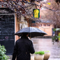 A lonely person walks a rainy day covering himself with an umbrella from bad weather.