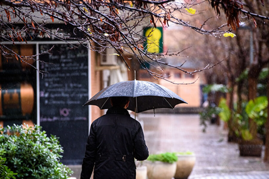 A lonely person walks a rainy day covering himself with an umbrella from bad weather.